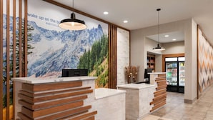 A reception area with wooden reception desks, a large mountain mural, and a refrigerator stocked with beverages. - La Quinta Inn & Suites by Wyndham Marysville (Marysville)