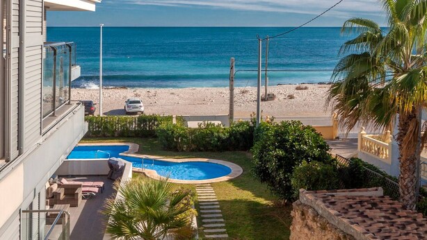 Ein modernes Haus mit Swimmingpool, Blick auf den Strand und einer Palme.