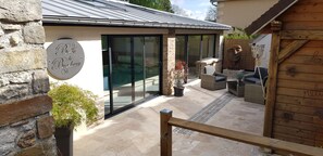 A modern building with a stone exterior, a glass door, and a wooden deck area with outdoor furniture. - L'ANNEXE, a charming vacation home in Champagne (Esternay)