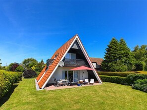 A modern house with a sloped roof, a patio with outdoor furniture, and a well-maintained garden. - Ferienhaus am Tief in Neuharlingersiel - Ferienhaus am Tief (Neuharlingersiel)