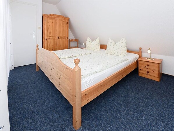A bedroom with a wooden bed, a nightstand, a wardrobe, and a door. - Ferienhaus am Tief in Neuharlingersiel - Ferienhaus am Tief (Neuharlingersiel)