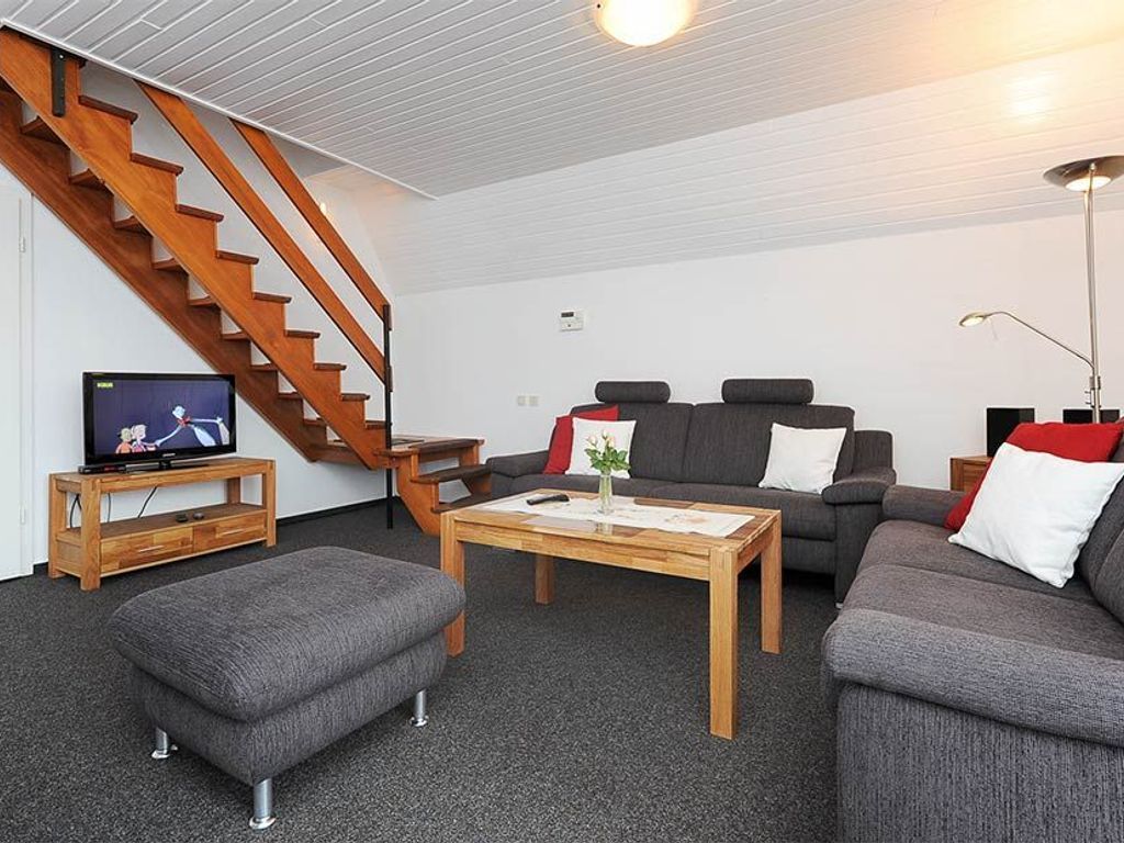 Een woonkamer met een trap, een televisie op een meubel, een bank, een poef en een salontafel.