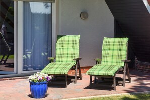 Two green plaid lounge chairs on a brick patio with a blue flower pot in front. - Ferienhaus am Tief in Neuharlingersiel - Ferienhaus am Tief (Neuharlingersiel)