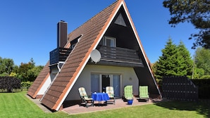 Een huis in de vorm van een driehoek, met een schuine dak, een schotelantenne en een terras met stoelen en een tafel.