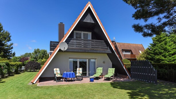 Een huis in driehoekige vorm met een schuin dak, een schotelantenne en een terras met twee stoelen en een tafel.