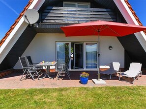An outdoor patio with a dining table, chairs, a red umbrella, and a satellite dish.