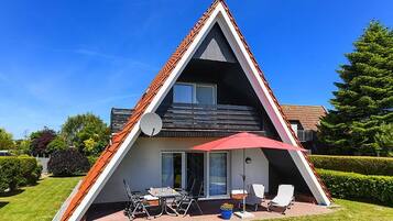 Een gebouw in een driehoekige vorm met een schuin dak, een terras met tuinmeubilair en een schotelantenne.