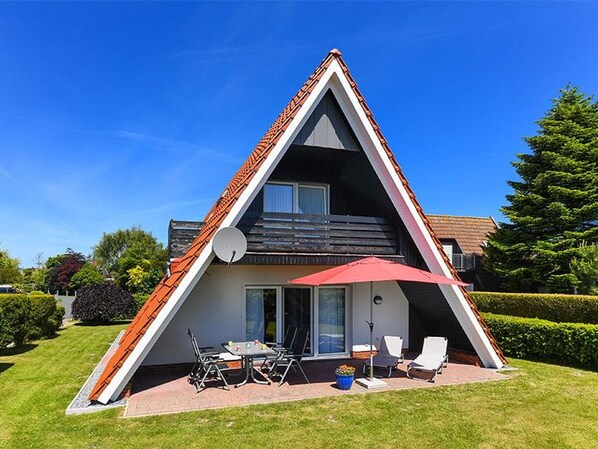 A triangular-shaped building with a sloped roof, a patio with outdoor furniture, and a satellite dish.