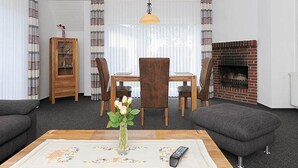 Een woonkamer met een open haard, een eettafel met stoelen, een bank en een salontafel met een bloevas.