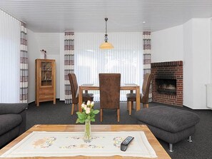 En stue med pejs, et spisebord med stole, en sofa og et sofabord med en vase blomster.