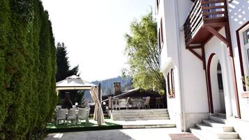 A building with a staircase leading to a covered outdoor seating area with chairs and tables.