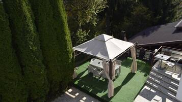 Un espacio de patio con mesa y sillas bajo un toldo, rodeado de follaje.