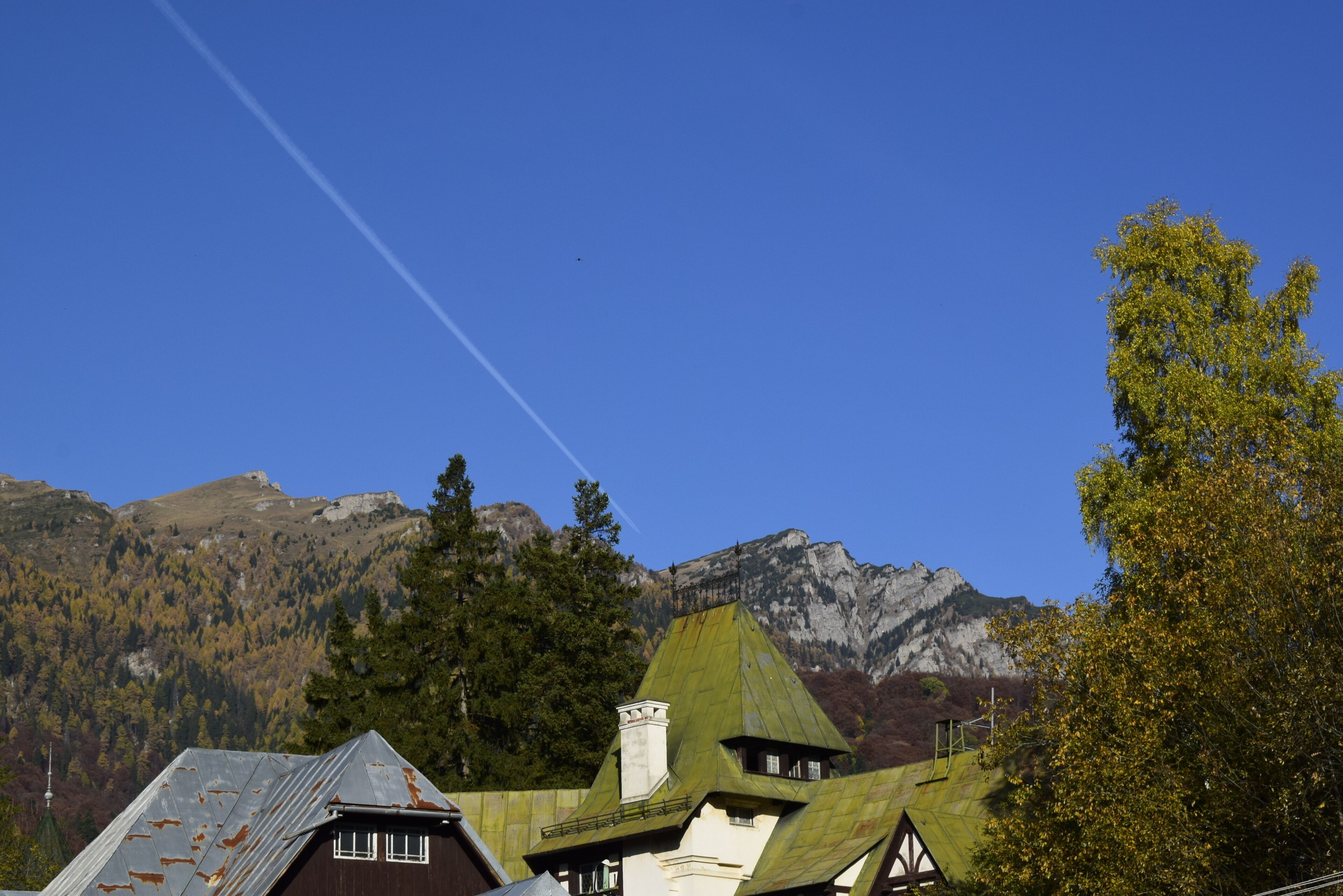 A mountain village with traditional houses, a clear sky, and a visible contrail.