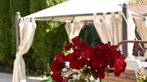 A gazebo with white curtains and red flowers in the foreground. - Pensiunea Nicolas (Sinaia)