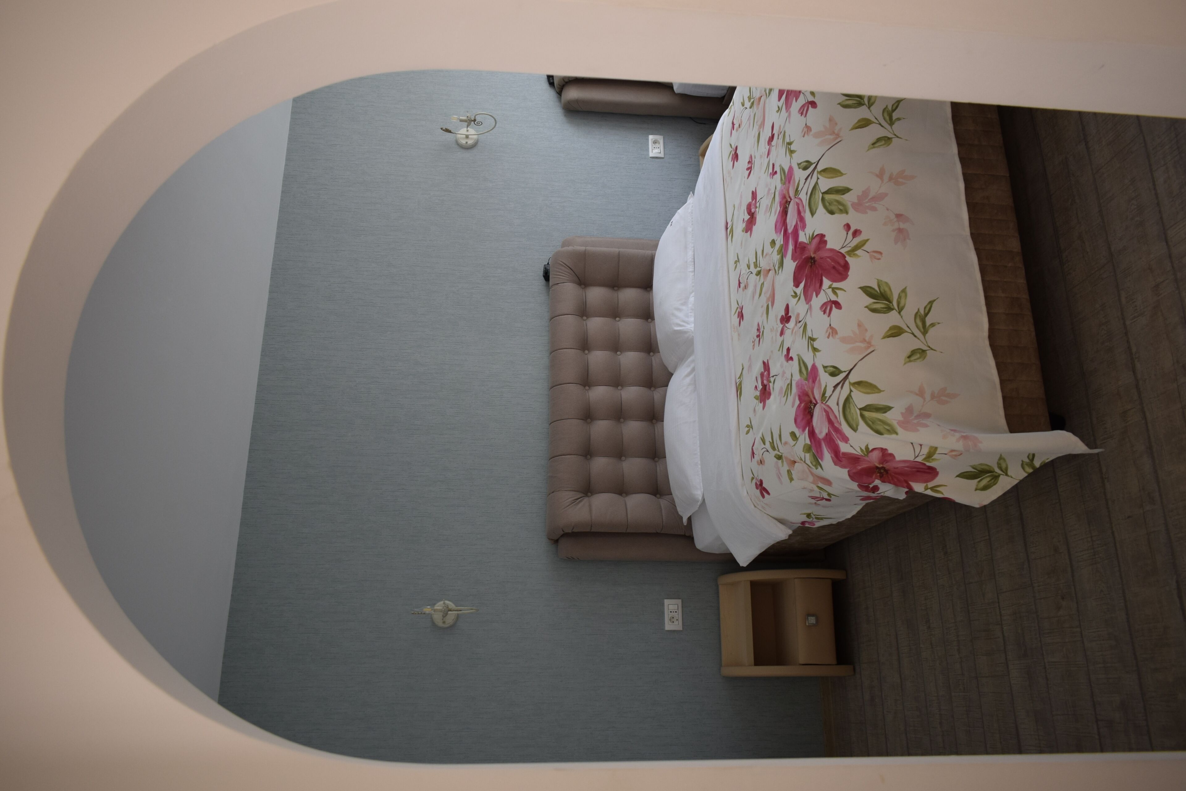 Un dormitorio con cama, mesita de noche, lámpara de pared y pequeño armario de madera.