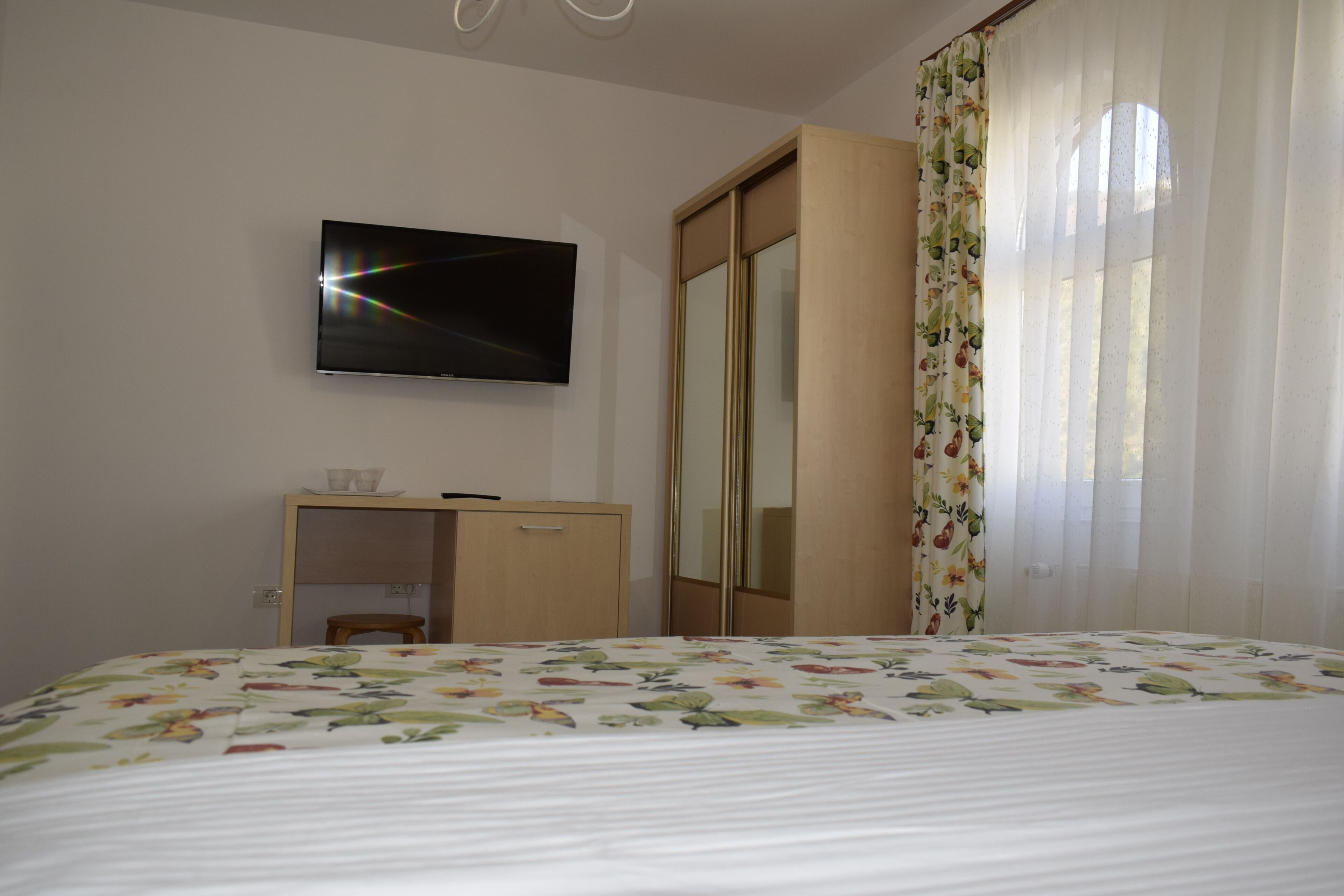 A bedroom with a bed, a TV mounted on the wall, a wooden wardrobe, and a mirror.