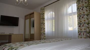 Een slaapkamer met een bed, een aan de muur bevestigde televisie, een kledingkast en een raam met bloemen gordijnen.