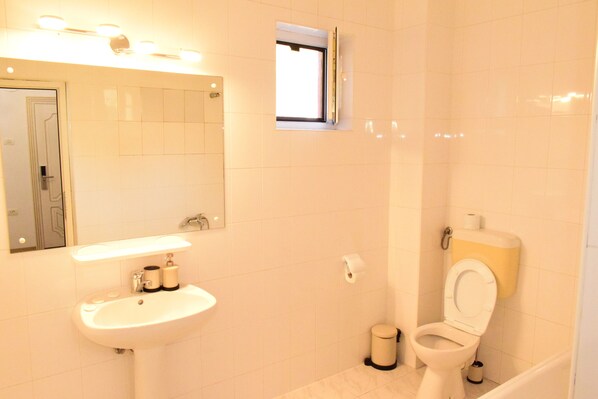 A bathroom with a sink, mirror, toilet, and a small window. - Pensiunea Nicolas (Sinaia)
