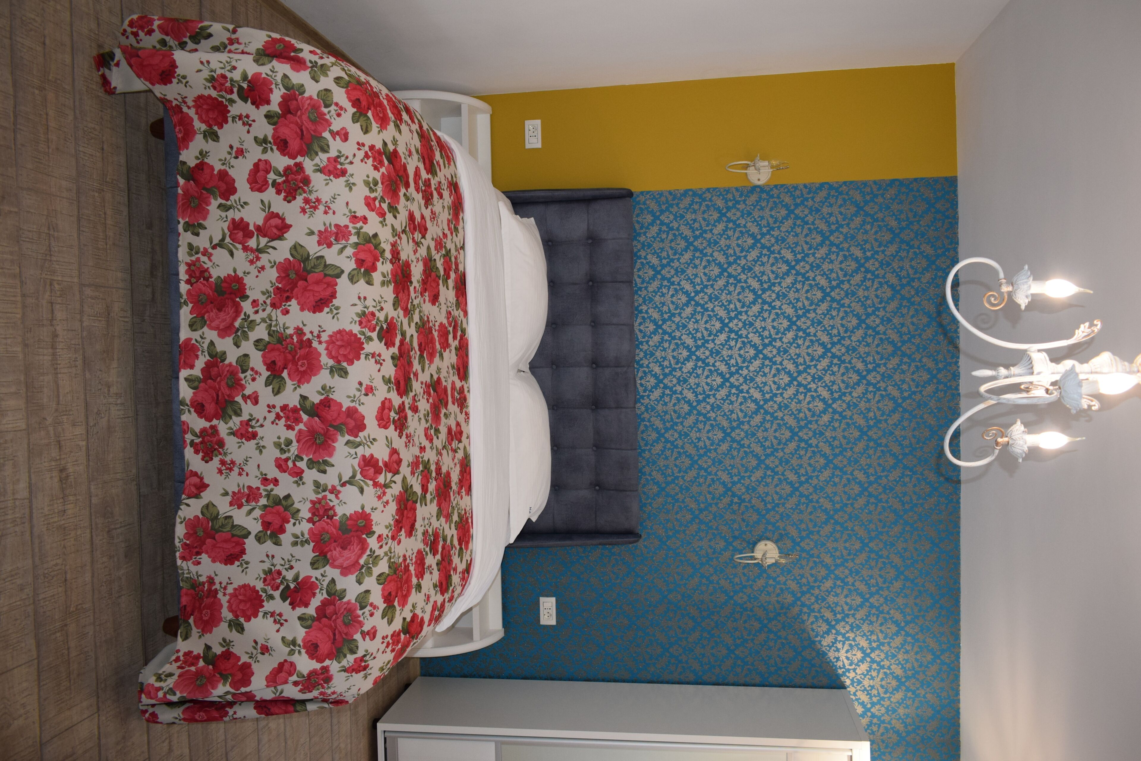 A bedroom with a bed, a nightstand, a wall-mounted light fixture, and a patterned wall.