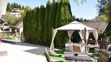 A patio area with a wooden table and chairs, a white canopy, and a green artificial turf.