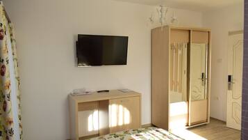 Een slaapkamer met een bed, een tv aan de muur, een kledingkast en een bureau met stoel.