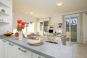 A modern kitchen with a dining area, a TV, and a balcony with a view.