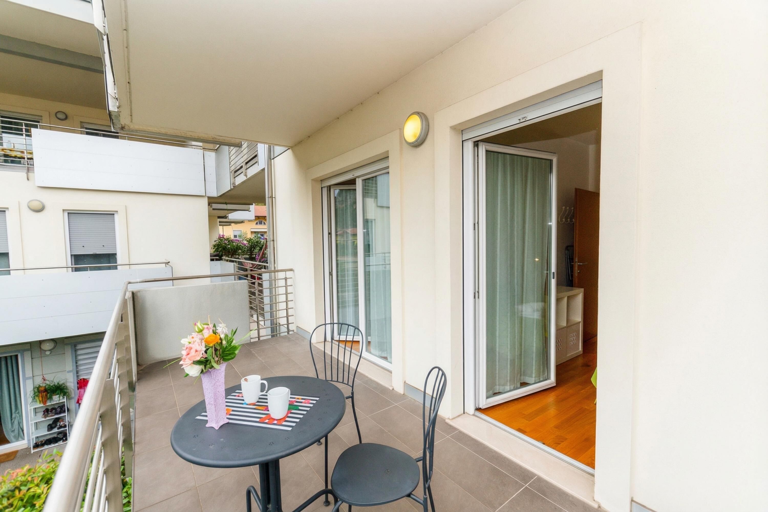 Ein Balkon mit Tisch und Stühlen, einem Blumentopf und einer Glastür zum Innenbereich.