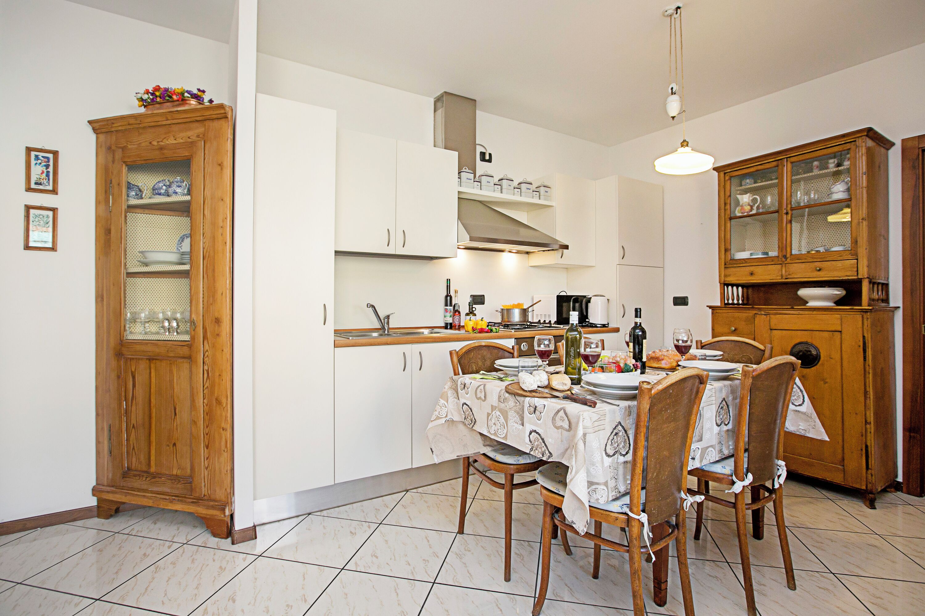 Une cuisine avec une table à manger pour quatre personnes, des meubles de rangement en bois et un sol carrelé.