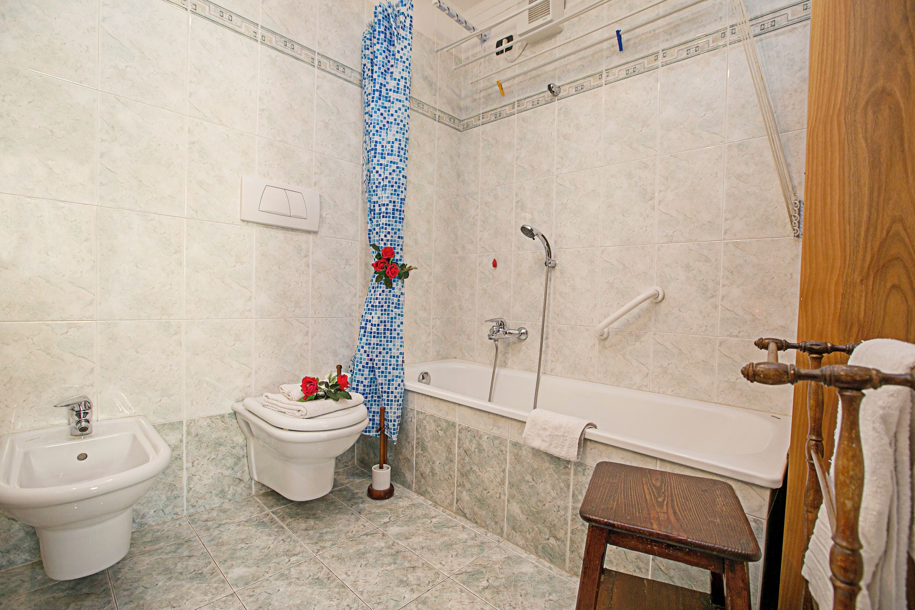 Een badkamer met een toilet, badkuip, een wc-bril en een houten kruk.