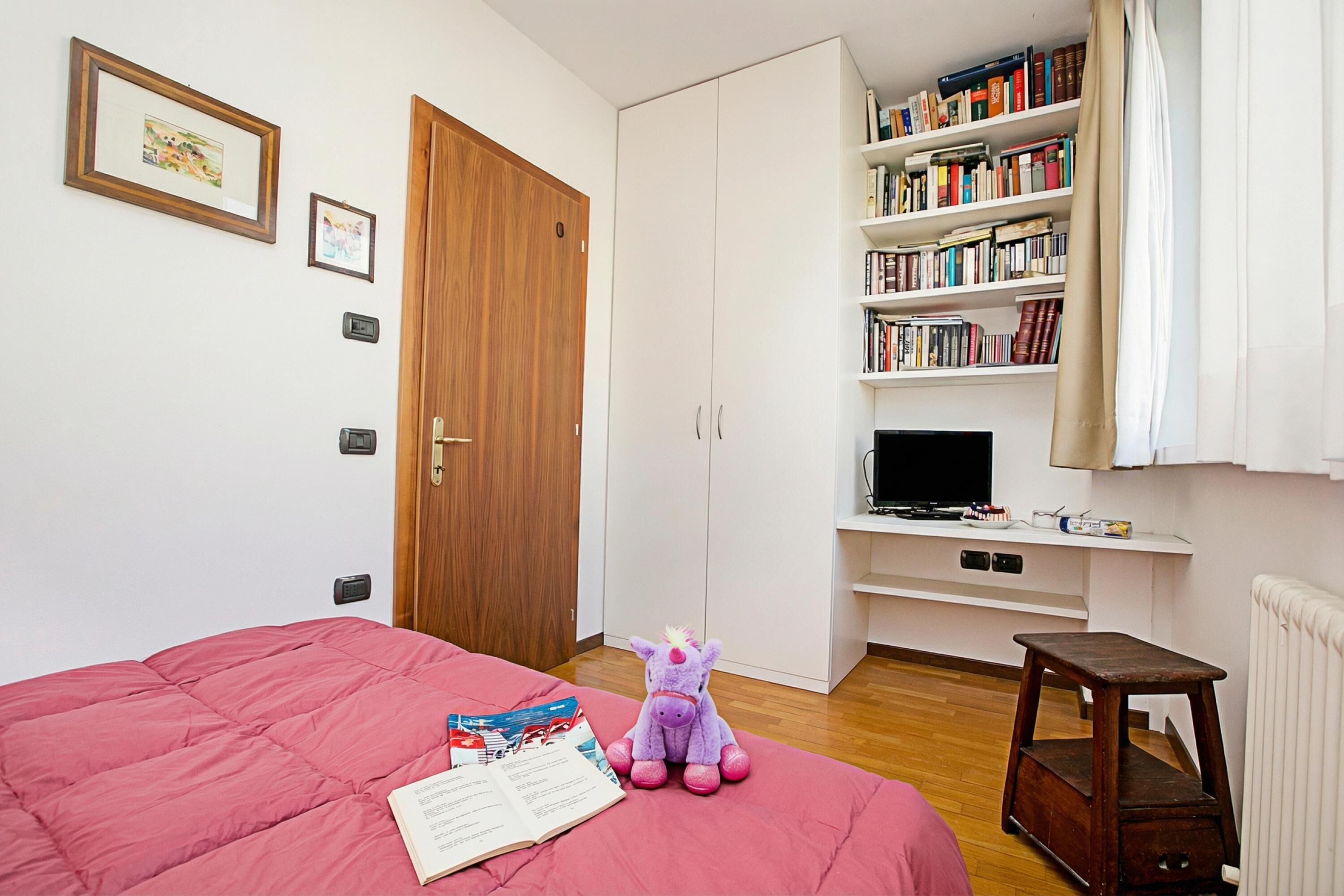 Un dormitorio con una cama, un juguete morado, una estantería y un televisor.