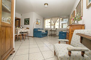 A living room with a dining table, blue sofa, patterned armchair, and a cabinet with glassware.
