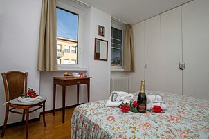A bedroom with a bed, a chair, a table, a window, and a radiator.