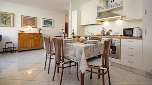 Un coin repas avec une table dressée pour quatre personnes, des chaises en bois, un lustre, une cuisine avec des meubles blancs et un four à micro-ondes.