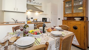 Une table à manger dressée avec des assiettes, des verres et une bouteille de vin, entourée de chaises et d’un buffet en bois doté de portes en verre.