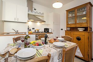 A dining table set with plates, glasses, and a bottle of wine, surrounded by chairs and a wooden cabinet with glass doors.