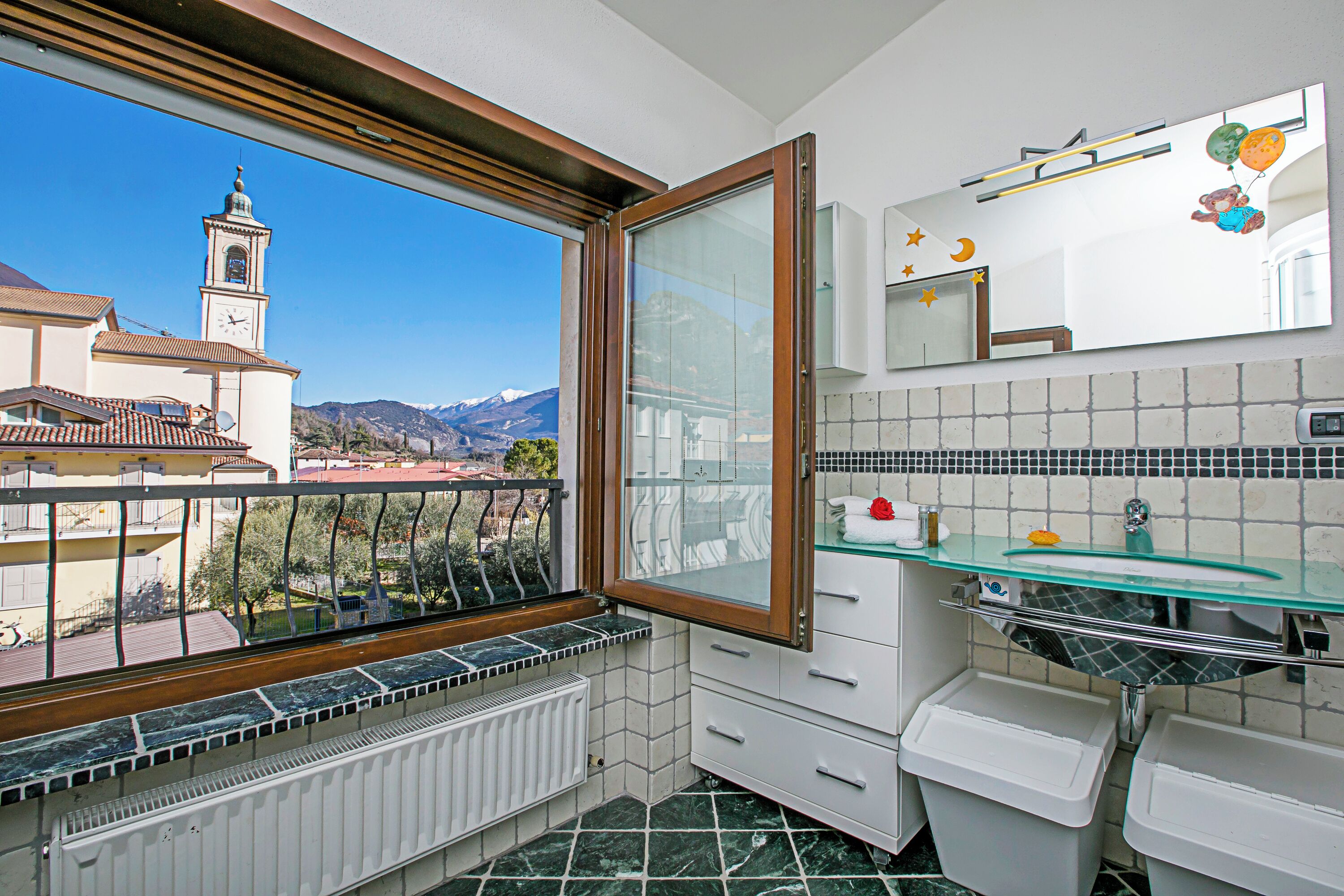 Ein Badezimmer mit Blick auf eine Kirche und Berge, ein Fenster und ein gefliester Boden.