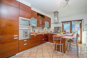 A modern kitchen with wooden cabinets, stainless steel appliances, and a bar area with stools. - Paulie Apartment (Riva del Garda)