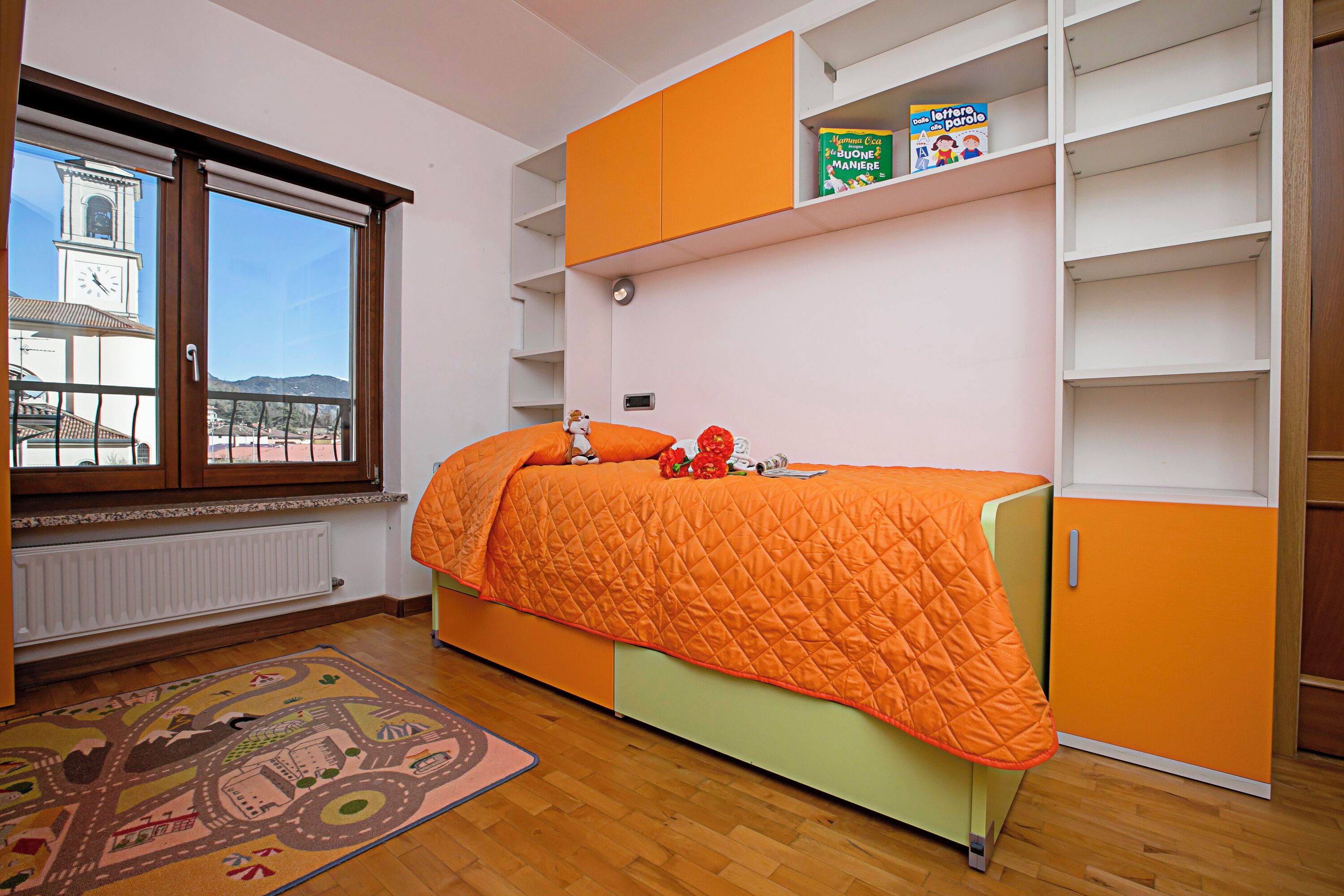 A bedroom with a bed, a radiator, a window, and a bookshelf.