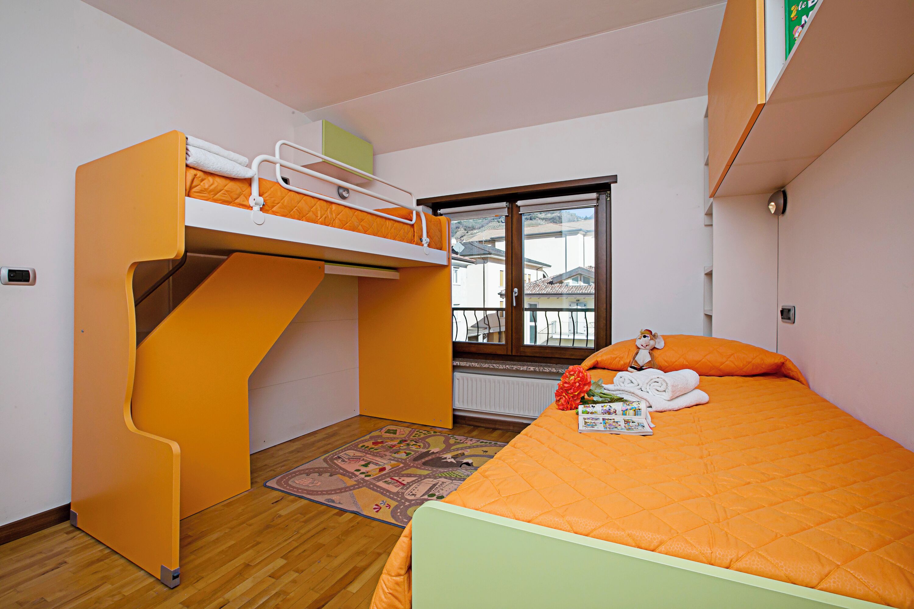 A room with a bunk bed, a window with a view, and a small table with a teddy bear.