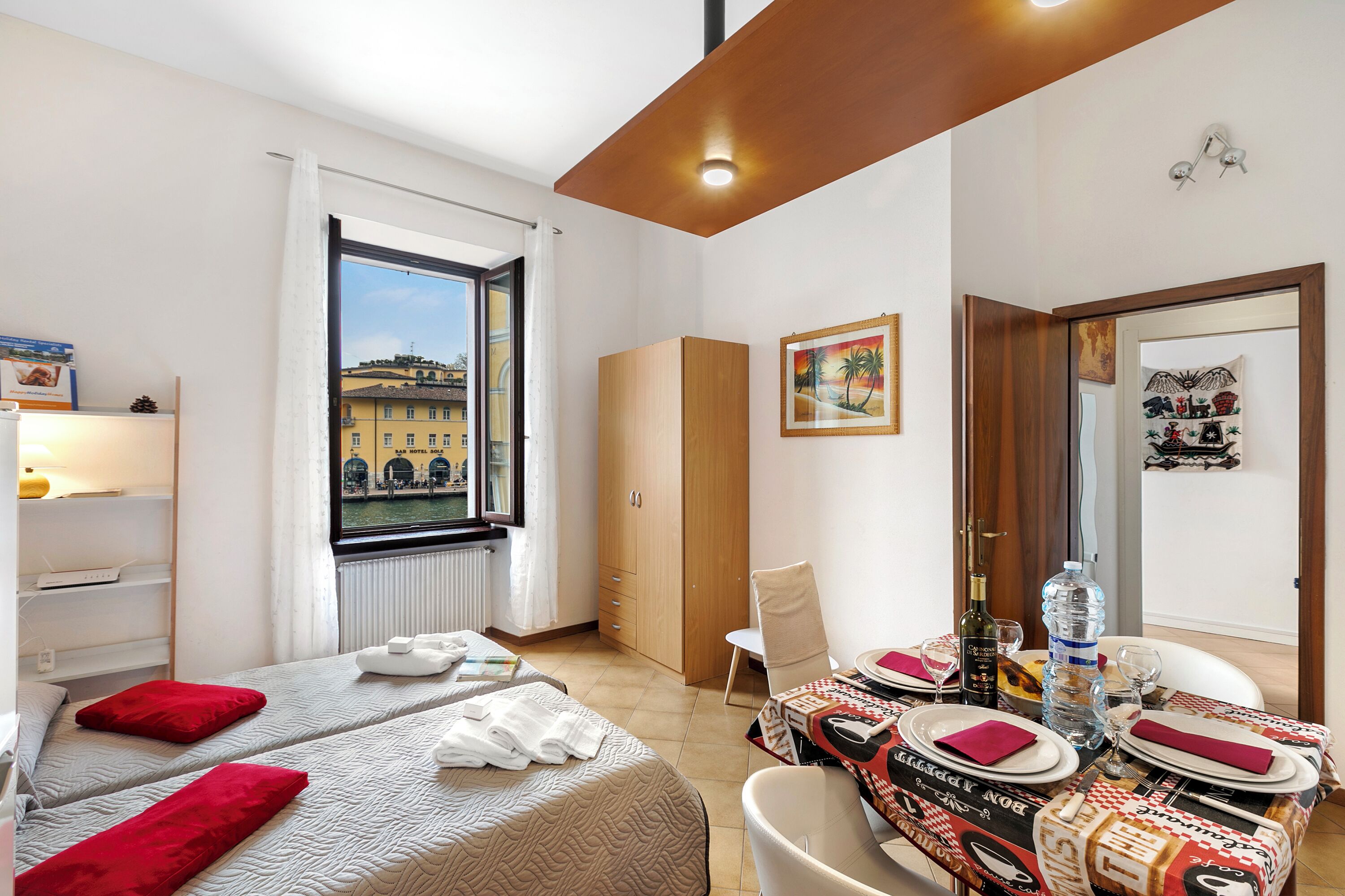 Una camera d'albergo con due letti, un tavolo da pranzo per due persone, una finestra con vista sugli edifici e un armadio.