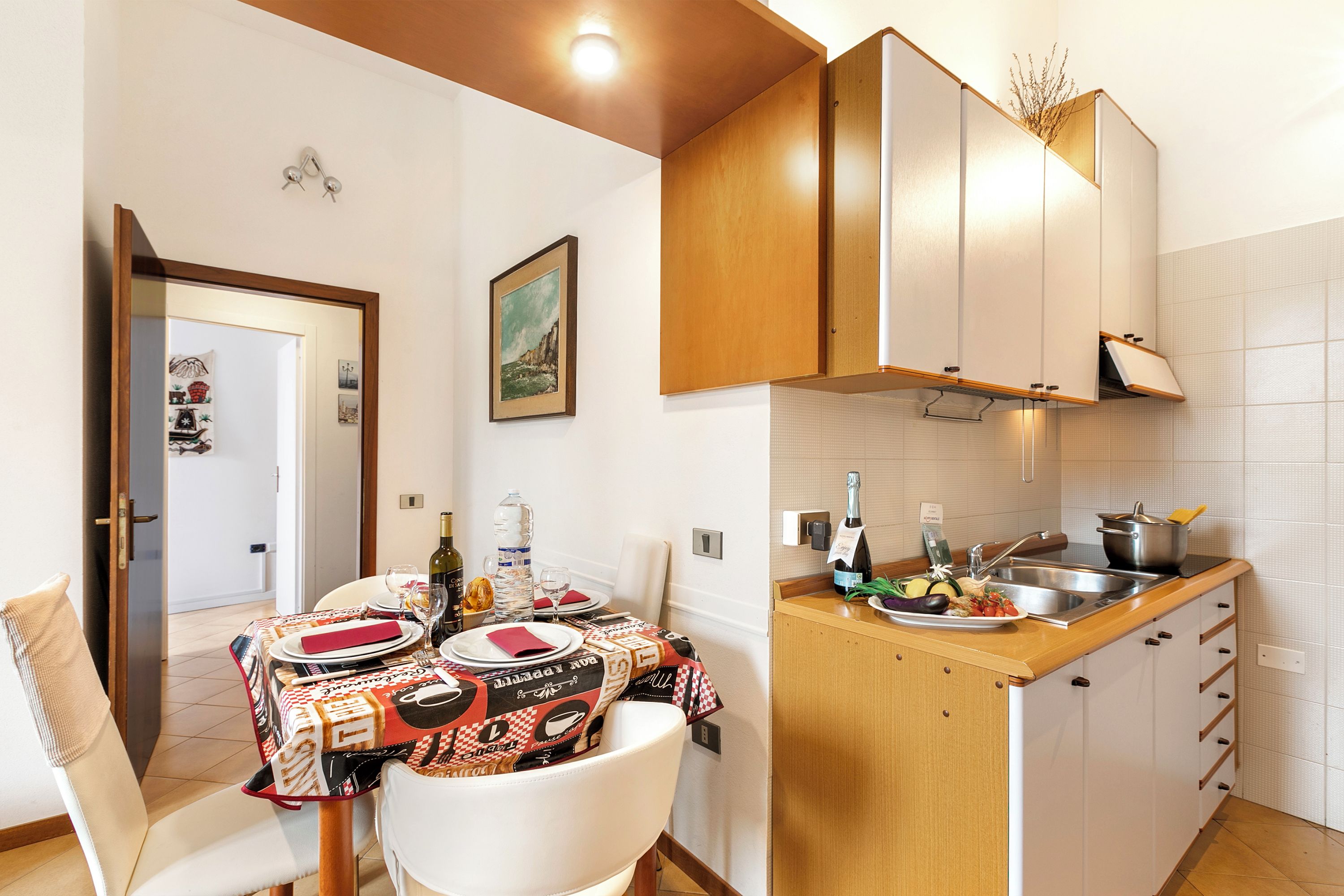 A compact kitchen with wooden cabinets, a dining table set for two, and a small island with a sink.