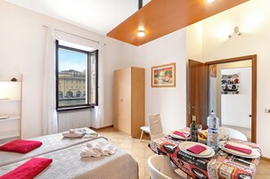 A hotel room with two beds, a dining table set with plates and glasses, a water bottle, and a bottle of wine.
