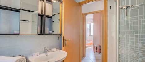 Une salle de bain moderne avec un lavabo blanc, un miroir et une douche en verre.