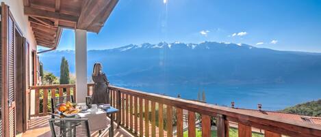 A balcony with a table set for breakfast, a wooden railing, and a mountainous view.