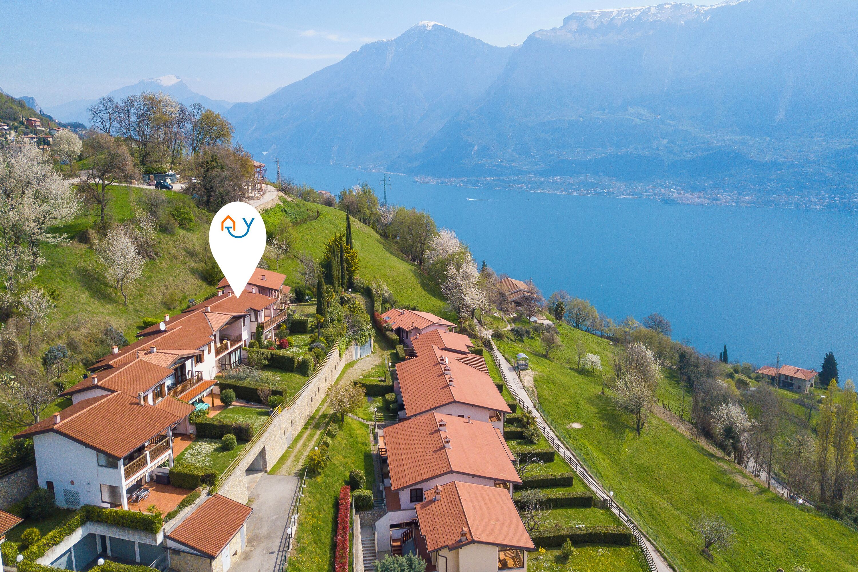 A residential area with houses on a hillside, a lake in the background, and a clear sky.