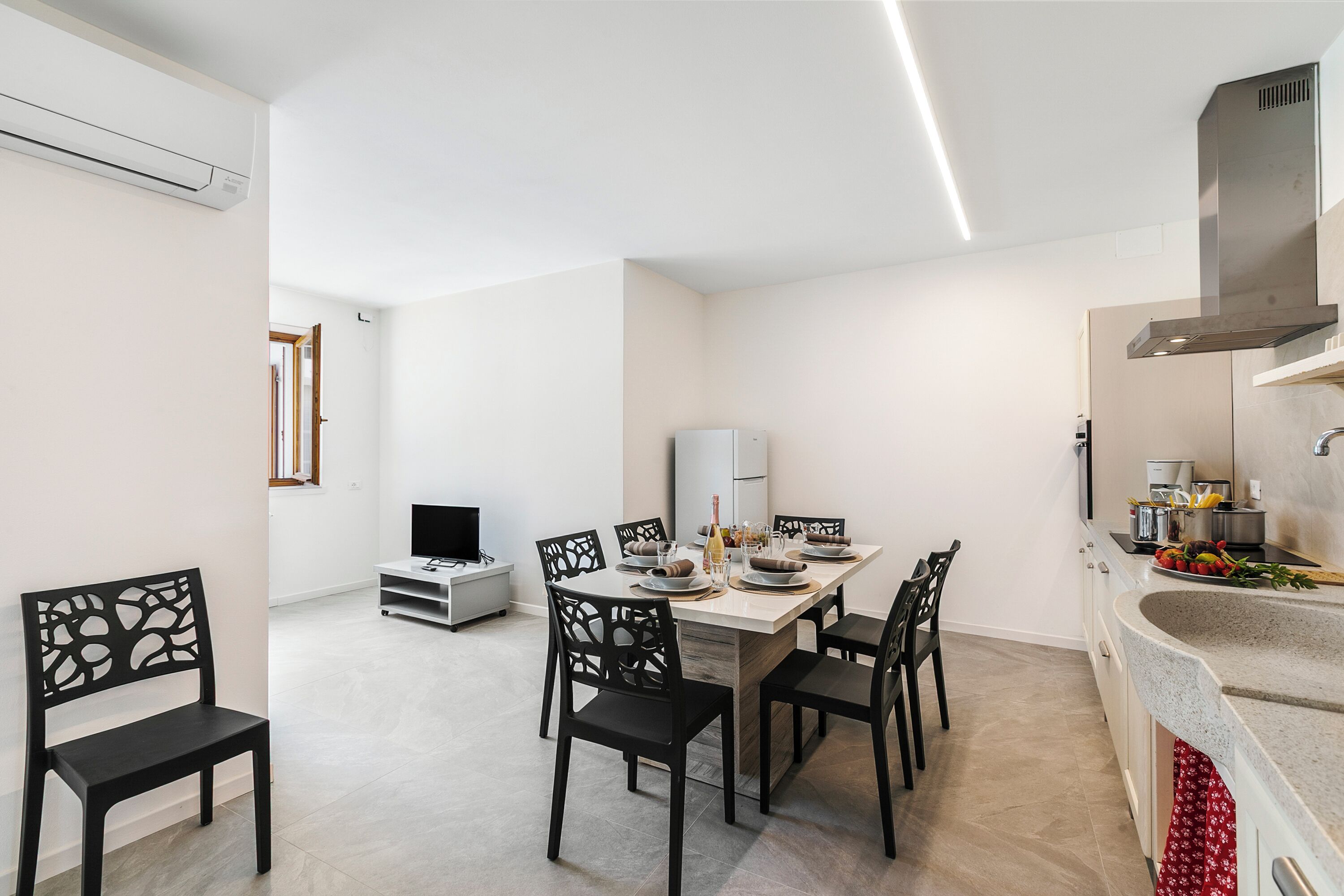 Una cocina moderna con una isla central, un comedor con seis sillas y un televisor al fondo.