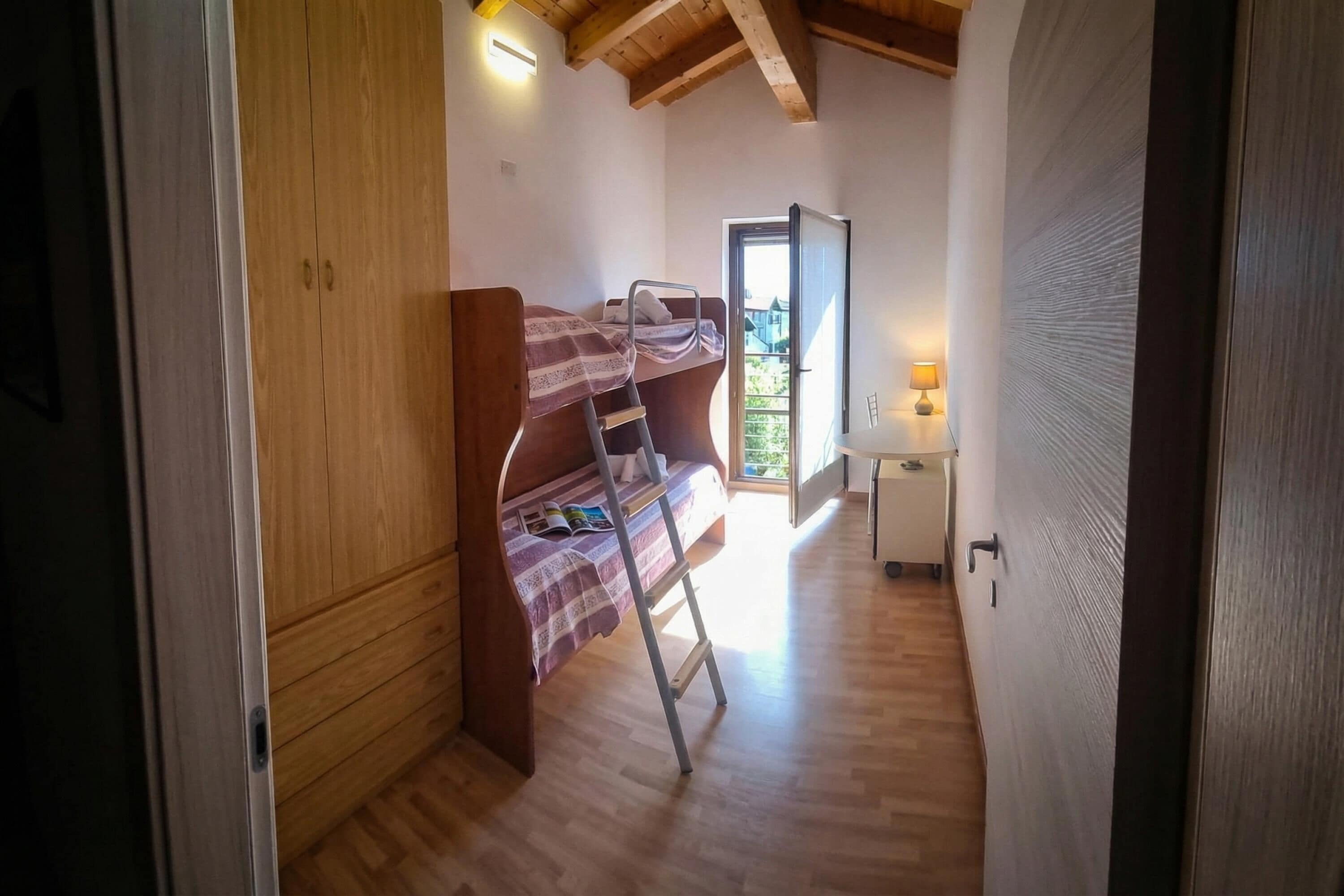 Una habitación con literas, un armario de madera y una mesita de noche con lámpara.