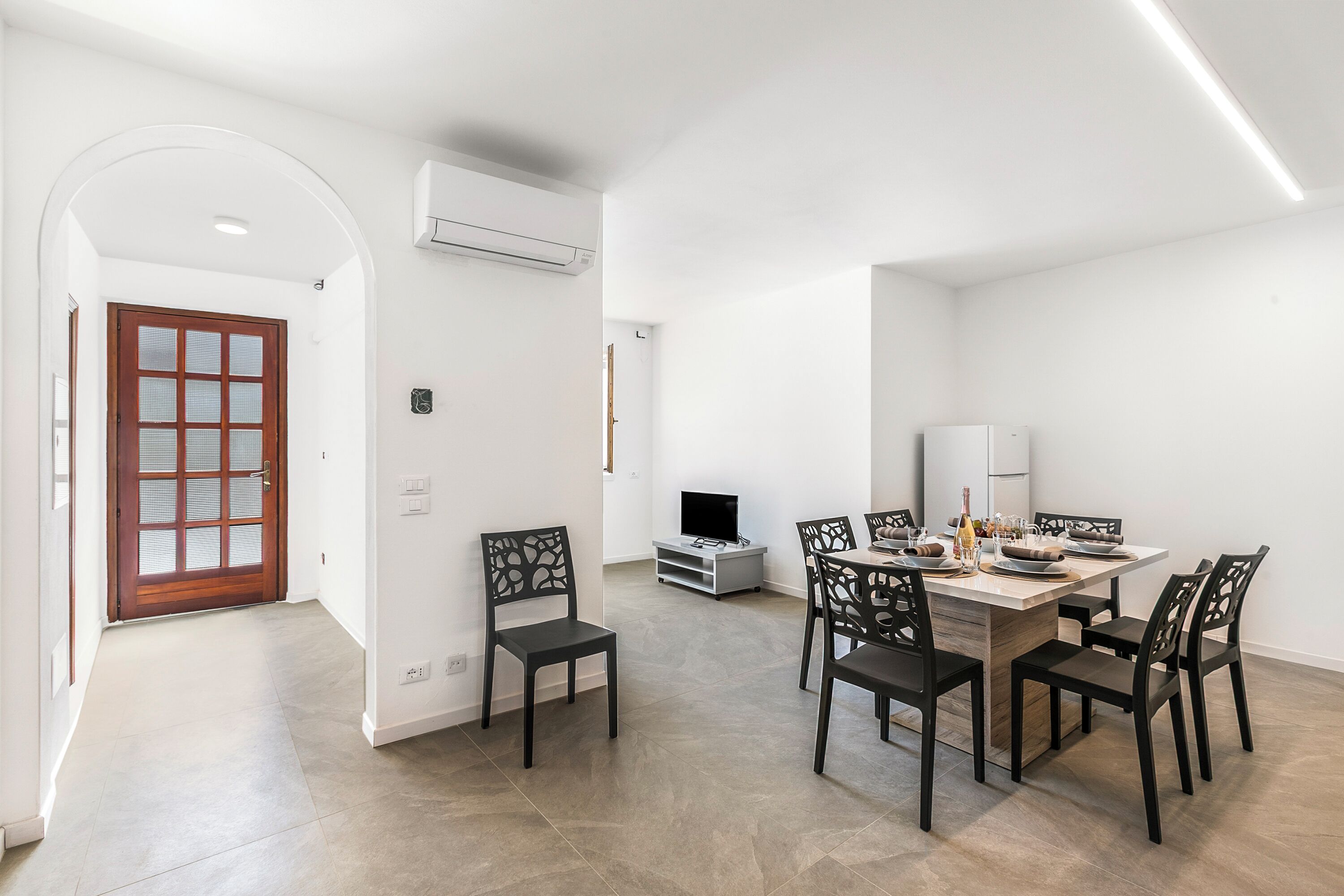 Un espace repas moderne comprenant une grande table et des chaises, un téléviseur et un réfrigérateur.