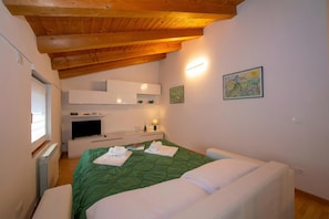 Ein Schlafzimmer mit Holzboden, einem Bett mit grüner Bettwäsche, einem Fernseher, einem Nachttisch mit Lampe und einem Bild an der Wand.