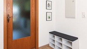 Una puerta de madera con un panel de vidrio esmerilado, un banco blanco con espacios de almacenamiento y dos cuadros en la pared.